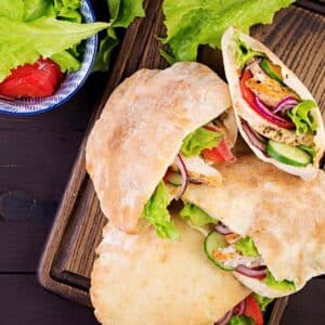 4 GREEK CHICKEN PITAS WITH LETTUCE, TOMATO AND RED ONION ON A CUTTING BOARD