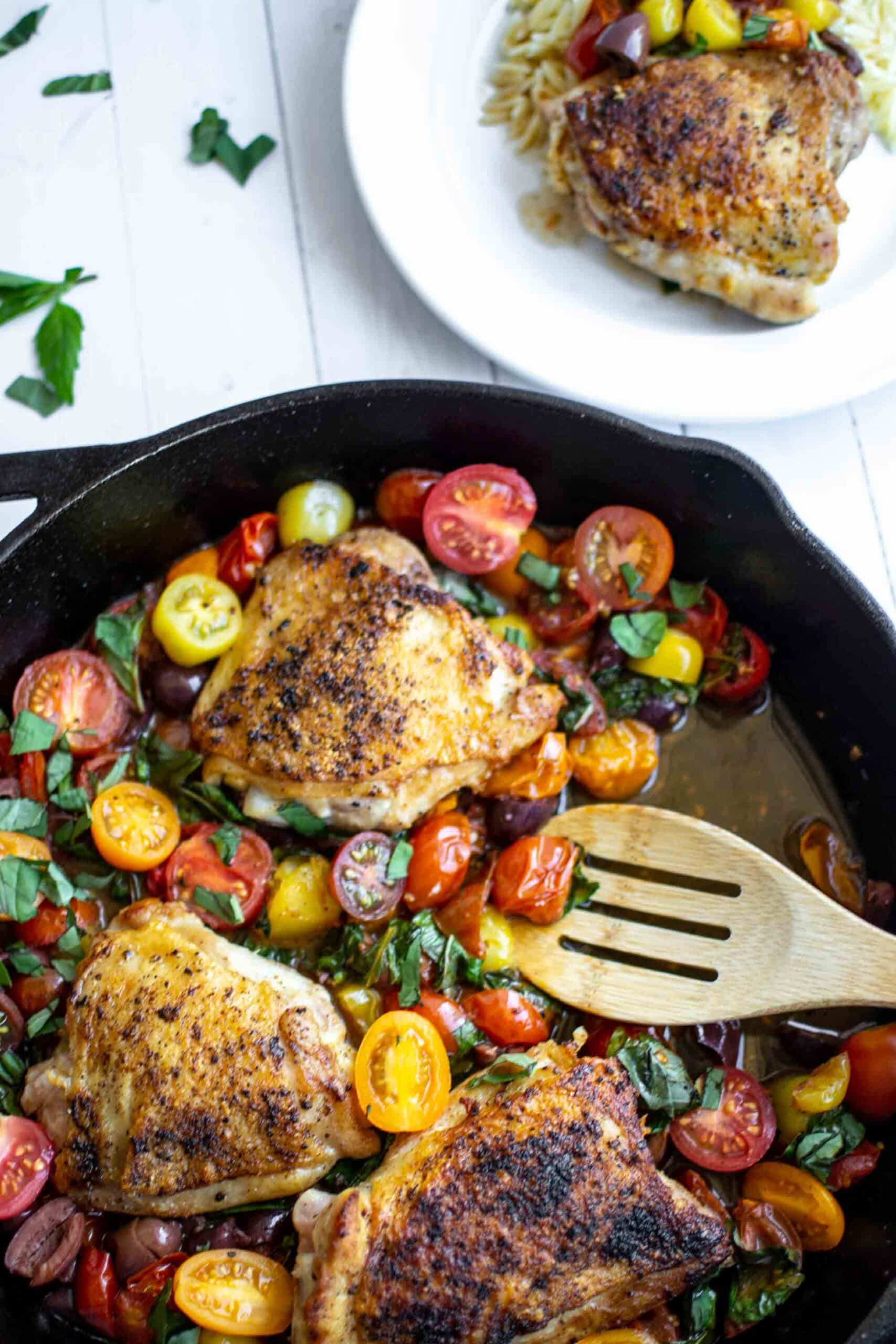Chicken thighs in a cast iron skillet with tomatoes and basil