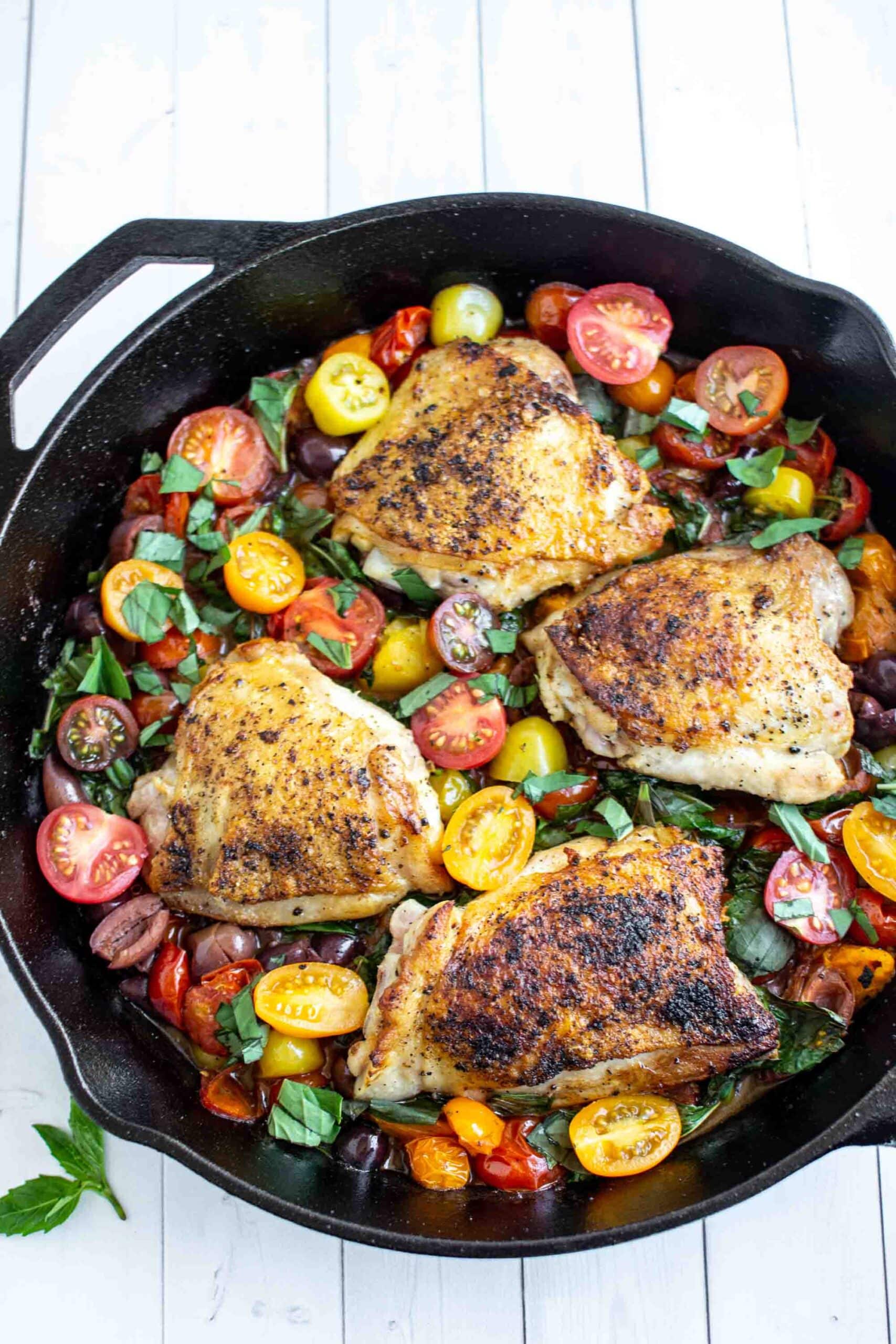 Chicken thighs in a cast iron pan with tomatoes and basil.