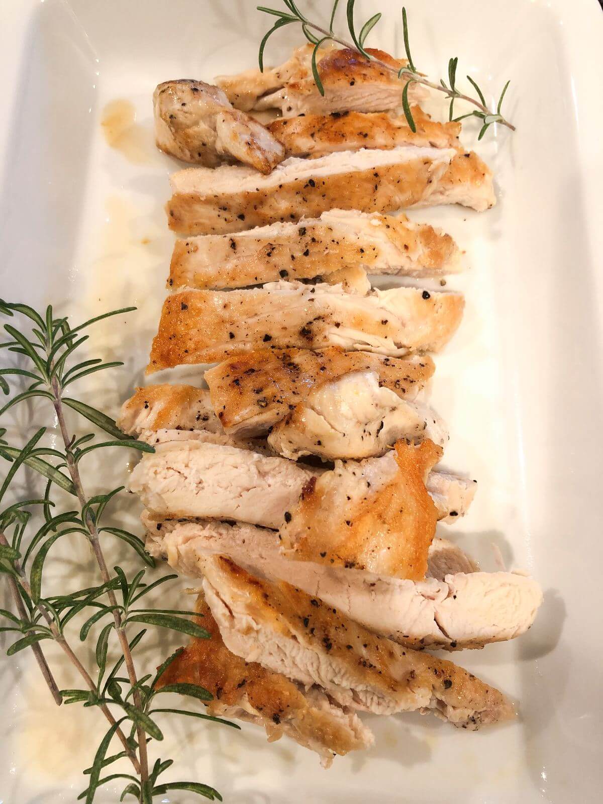 Cooked chicken on a white plate with rosemary