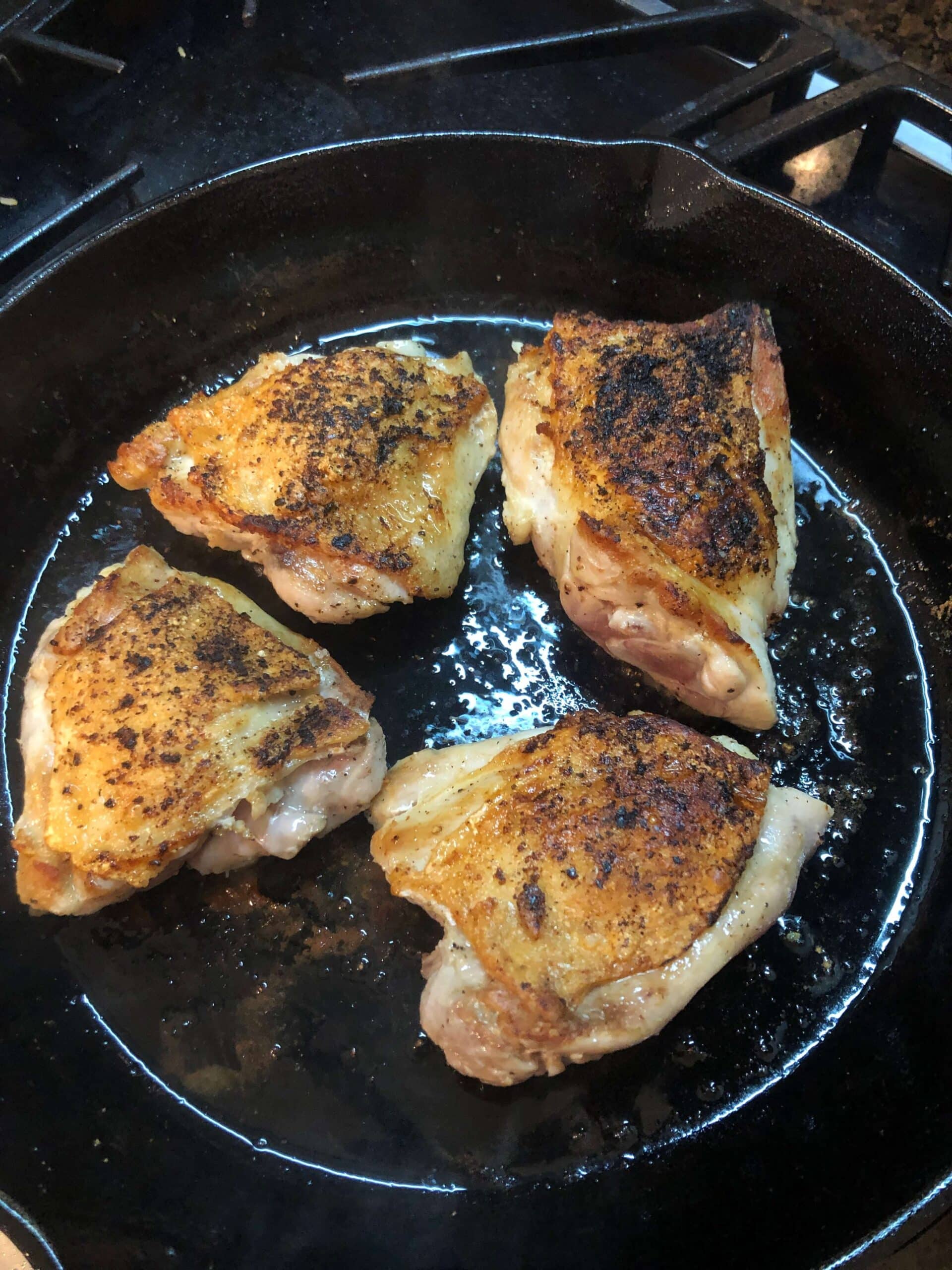 Chicken thighs cooking in cast iron skillet