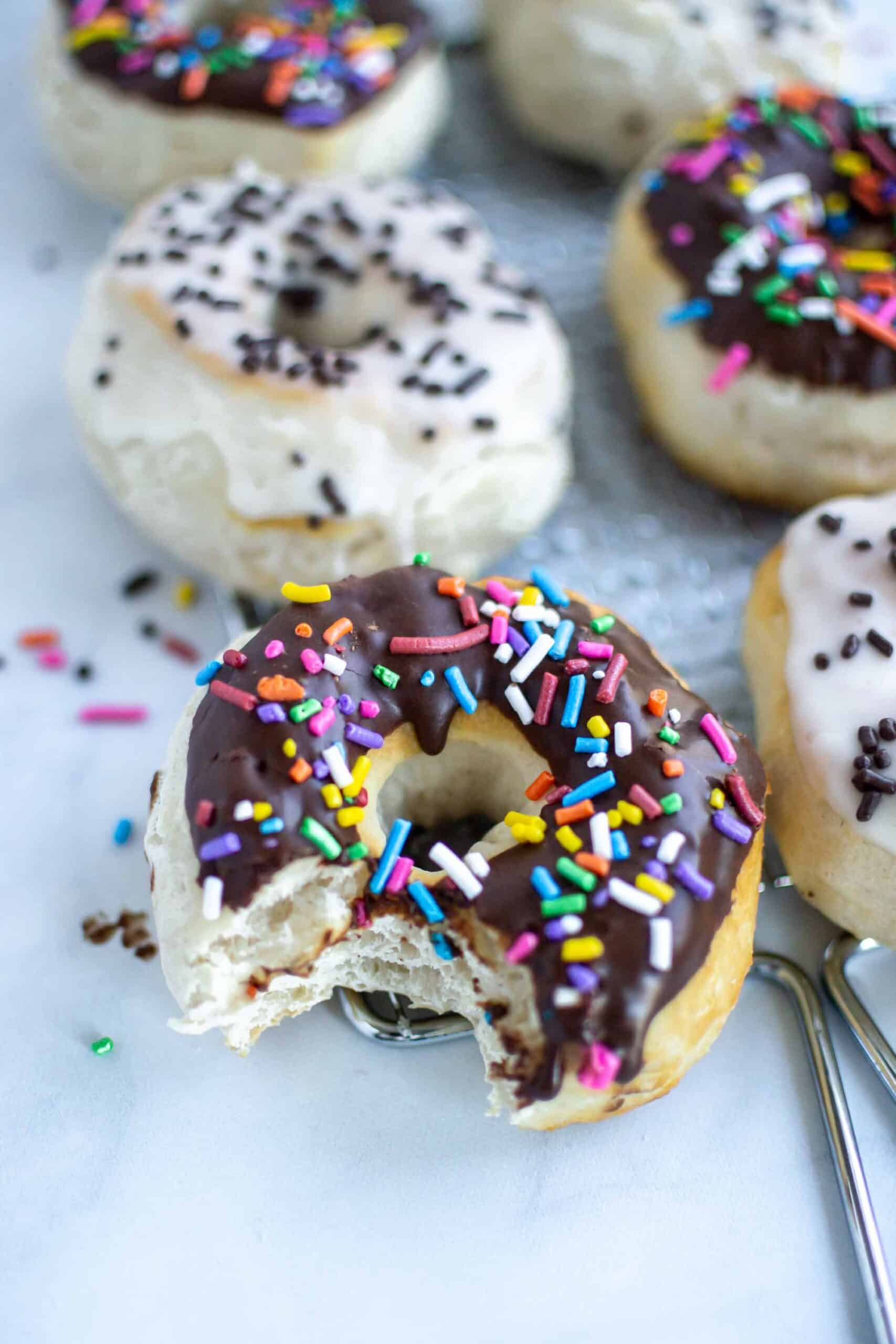 Chocolate and vanilla glazed air fryer biscuit doughnuts with sprinkles and chocolate doughnut with a bite taken.