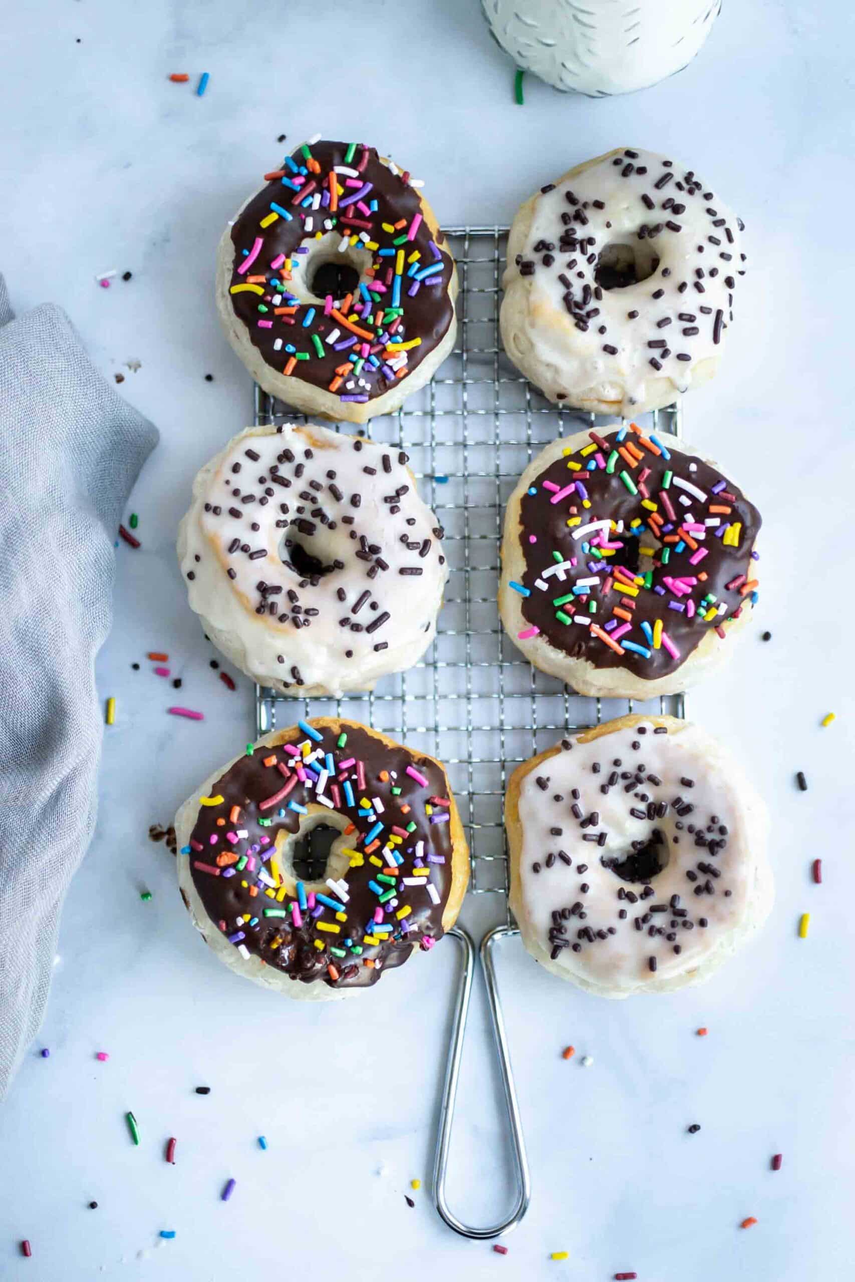 Chocolate and vanilla glazed air fryer biscuit doughnuts with sprinkles and chocolate sauce.