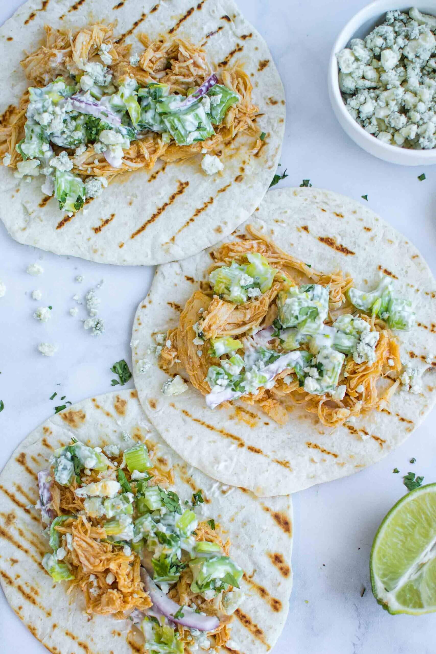 Three buffalo chicken tacos on a plate with blue cheese 