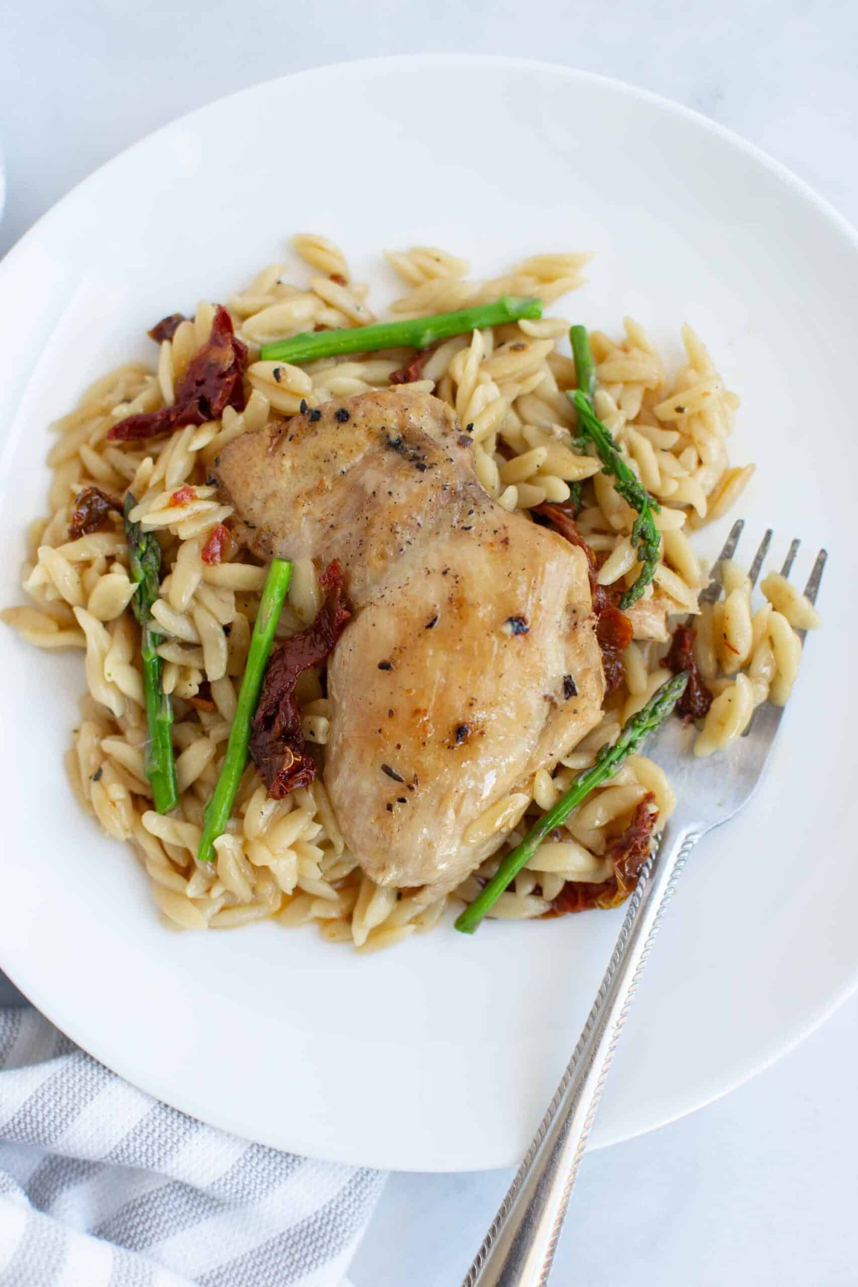 Creamy chicken with sun dried tomatoes and asparagus on a plate with a fork