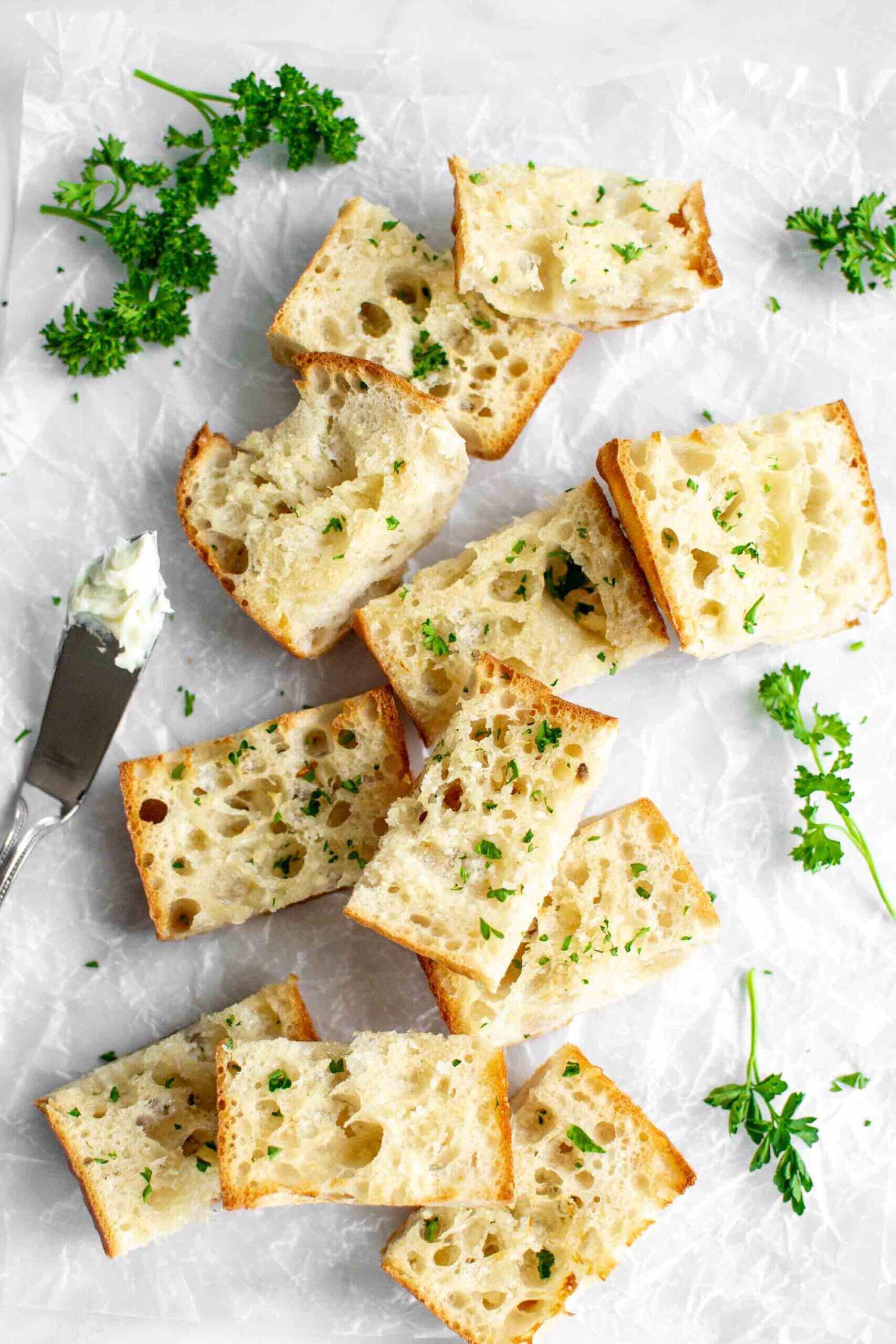 Pieces of air fryer garlic bread on a cutting board with parsley and a butter knife.