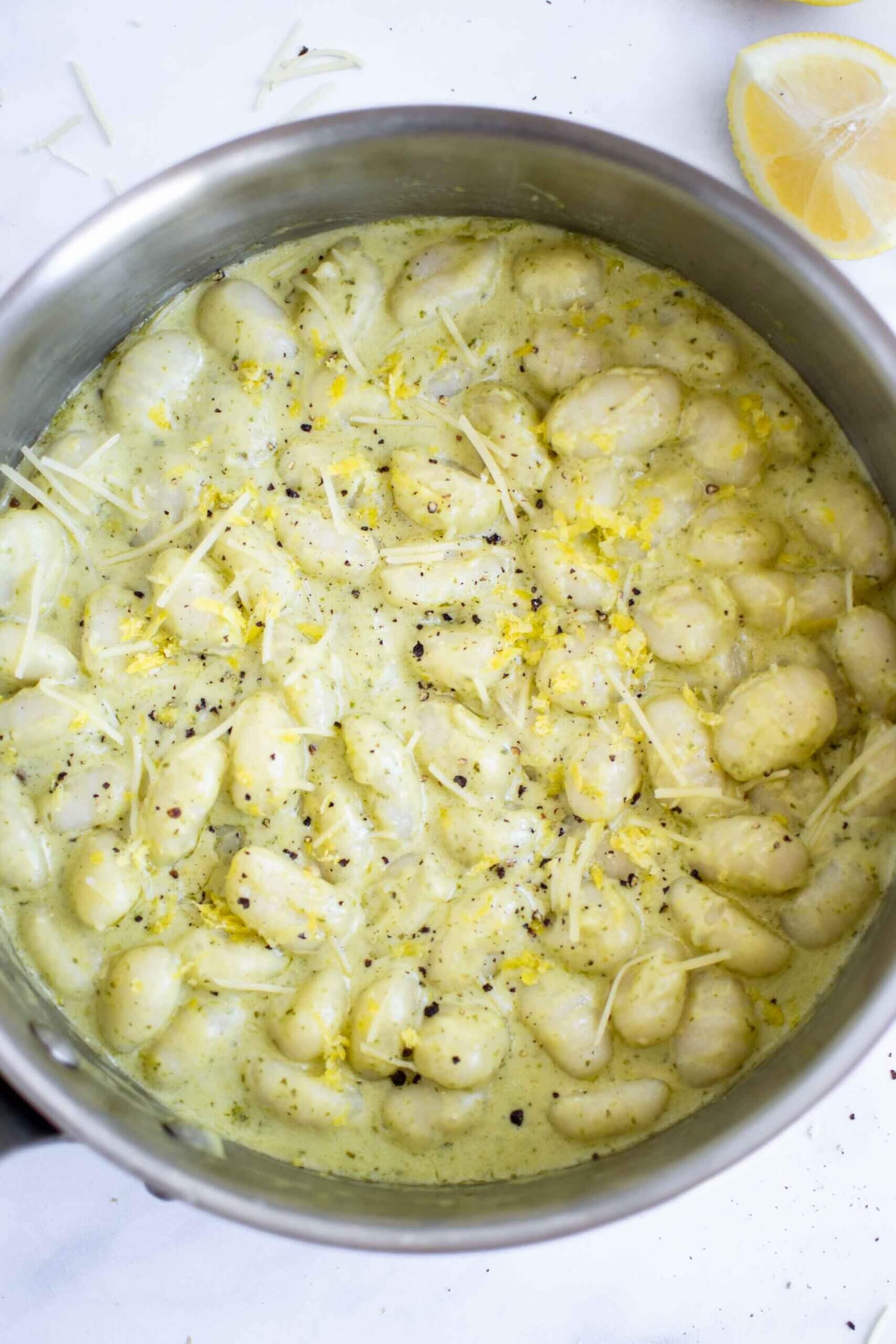 Creamy Lemon Pesto Gnocchi in a pan with black pepper, parmesan and lemon zest.