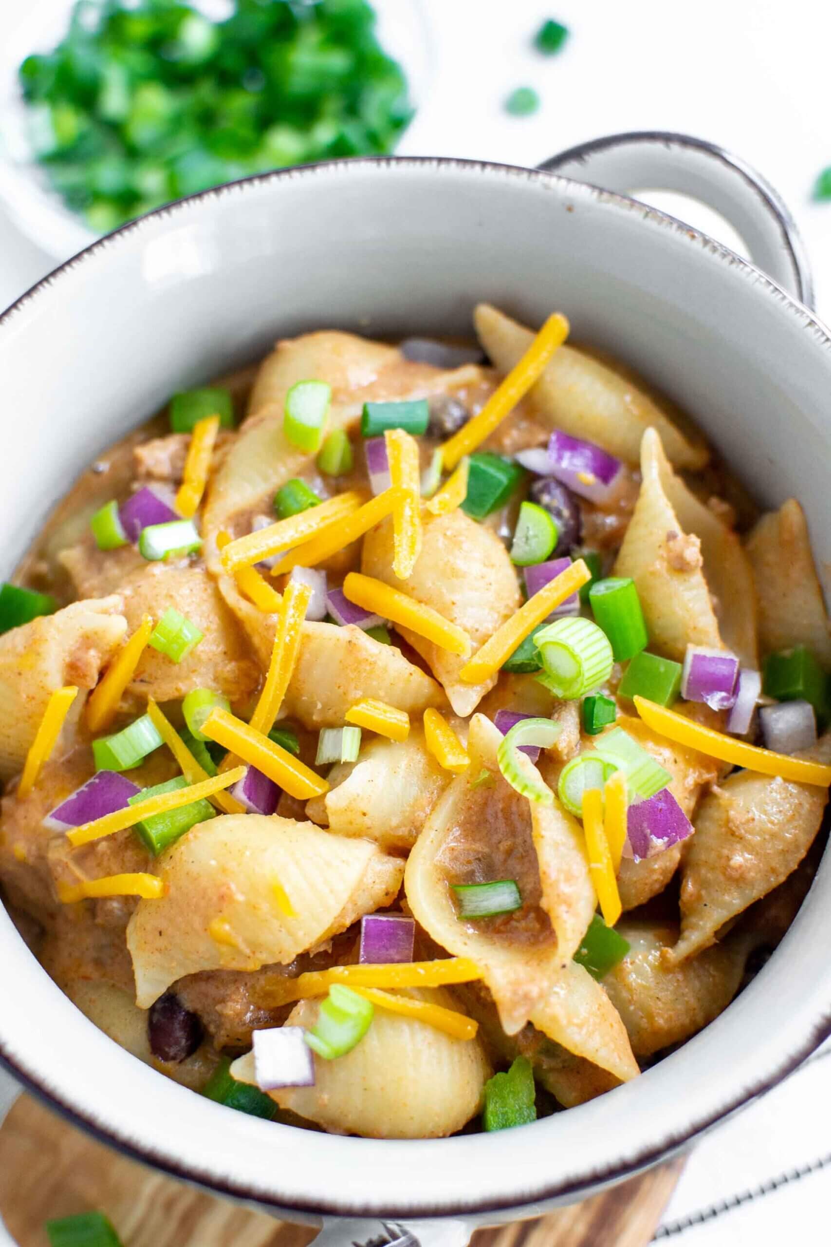 Creamy Crockpot Taco Pasta in a bowl topped with red onion, cheese and scallions.