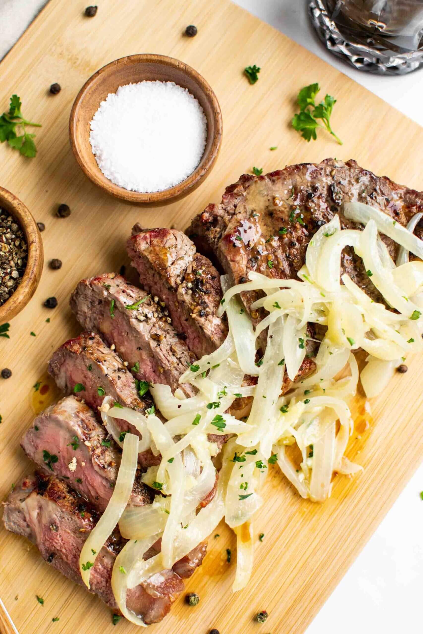 Steak with Garlic Butter Onions on a cutting board with salt and pepper