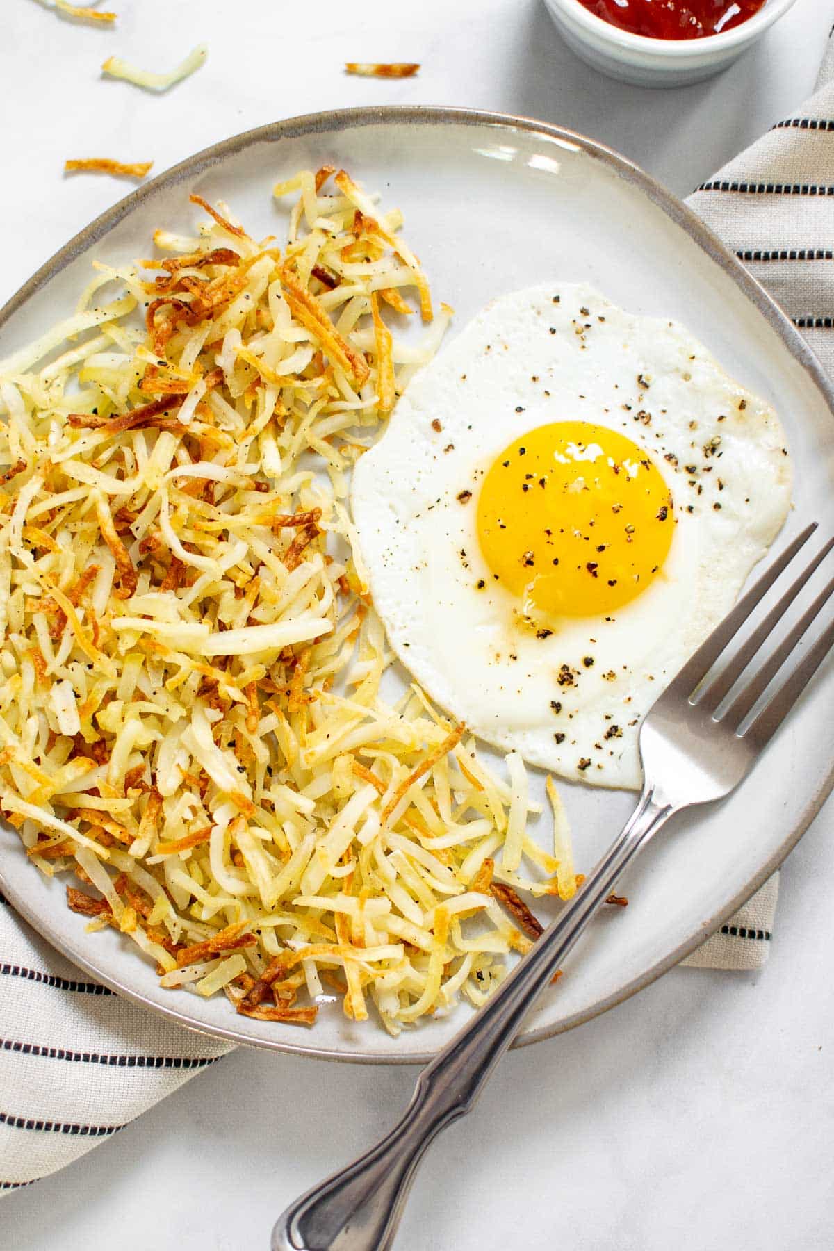 Hash browns on a plate with a fried egg and a fork. 