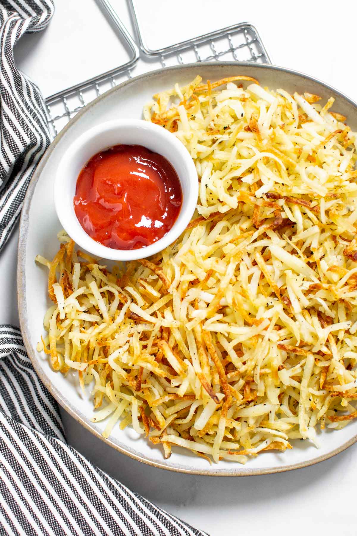 Hash browns cooked in the air fryer on a plate with a small bowl of ketchup.