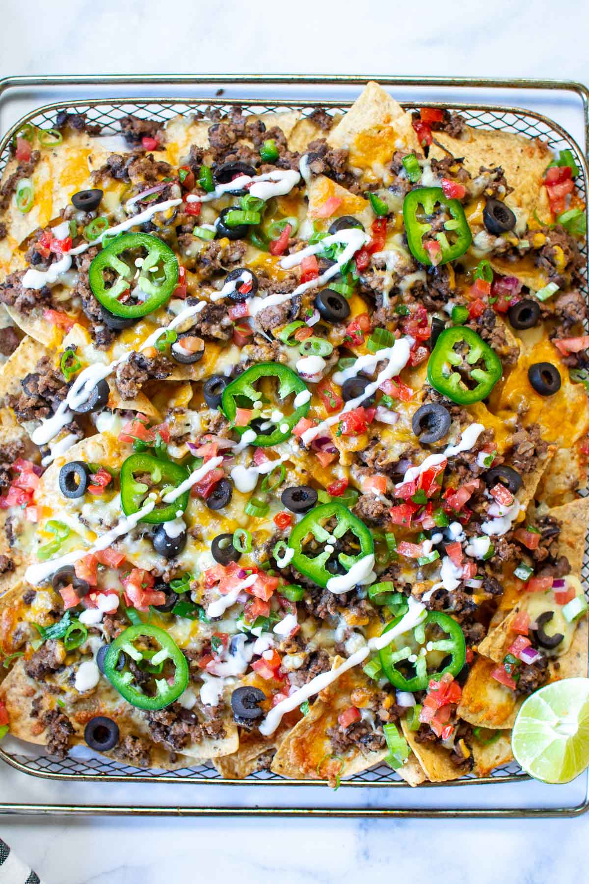 An air fryer tray of nachos  topped with ground beef, olives, salsa and sour cream.