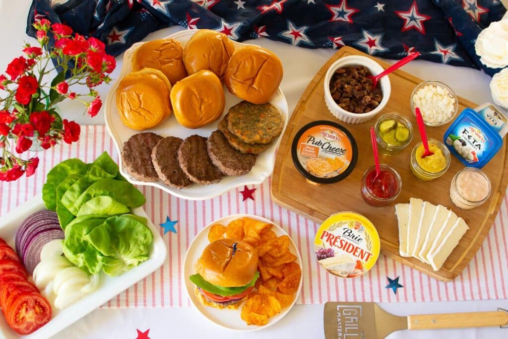 Burger bar set up with burgers, buns and condiments and 4th of July decorations.