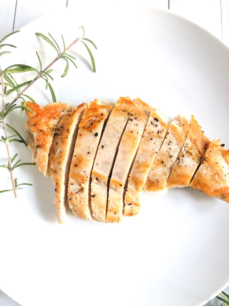 Cooked chicken breast on a white plate with rosemary.