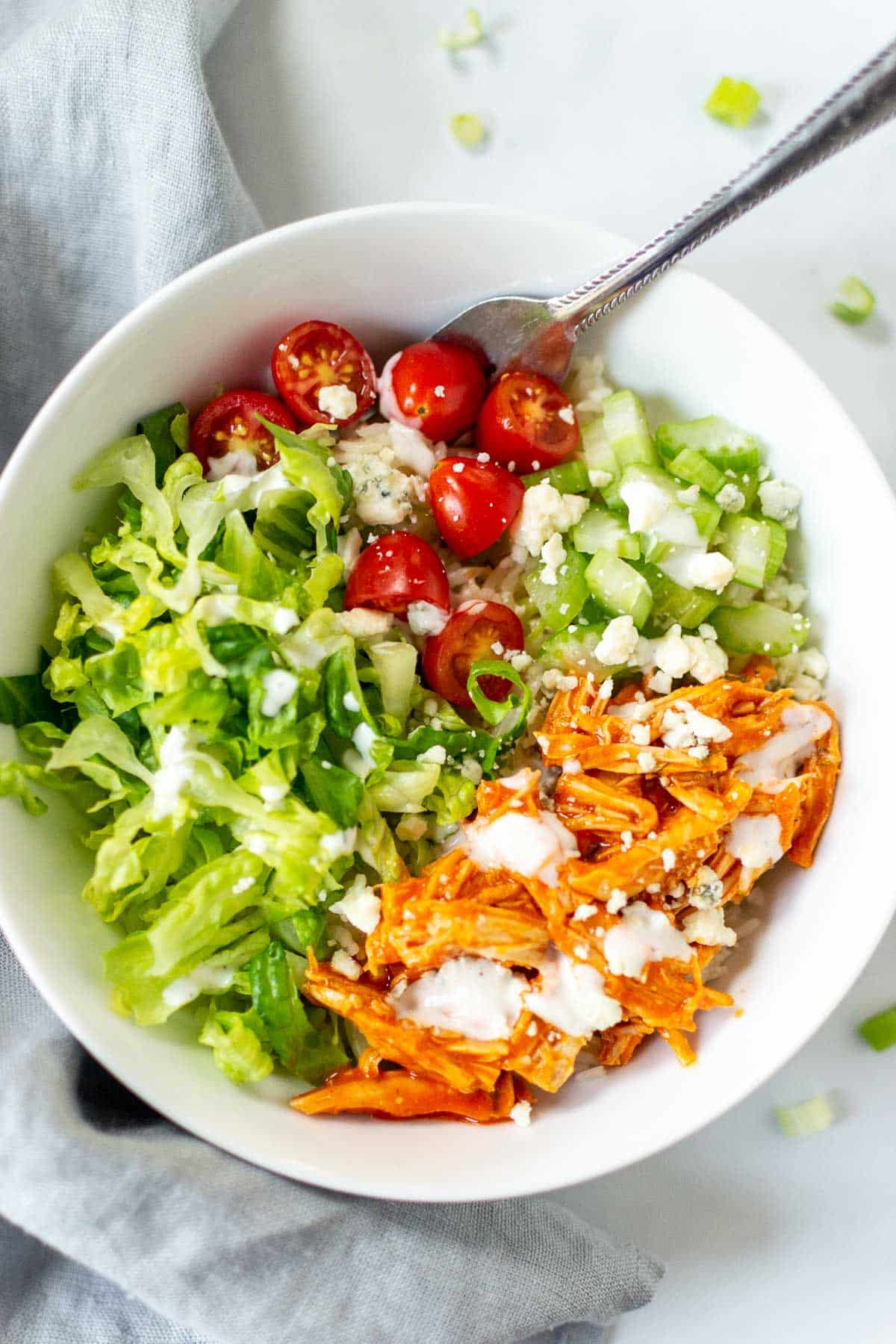 Buffalo chicken with veggies in a bowl topped with blue cheese and ranch dressing. 