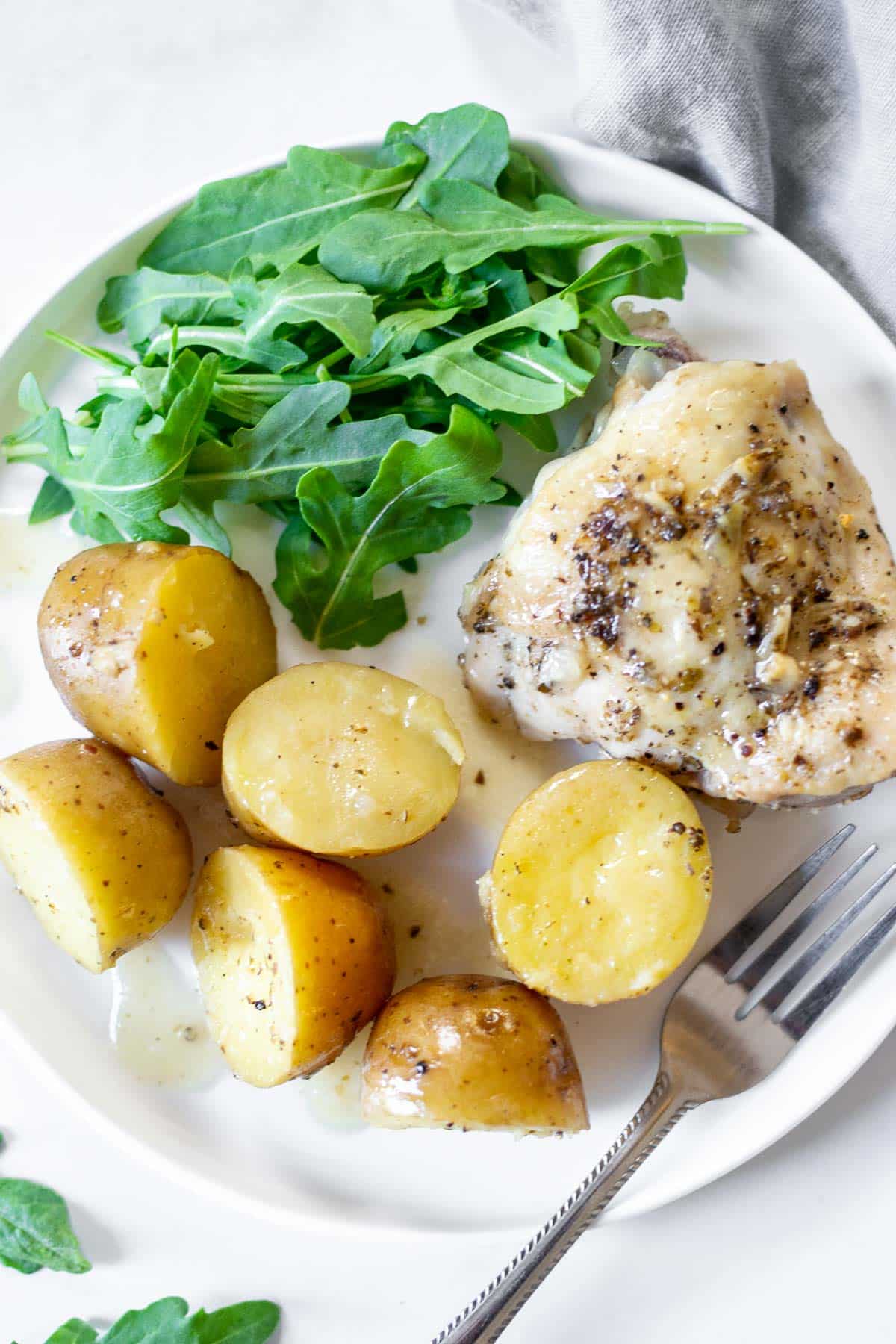 Chicken thighs, potatoes, arugula on a dinner plate with a fork.