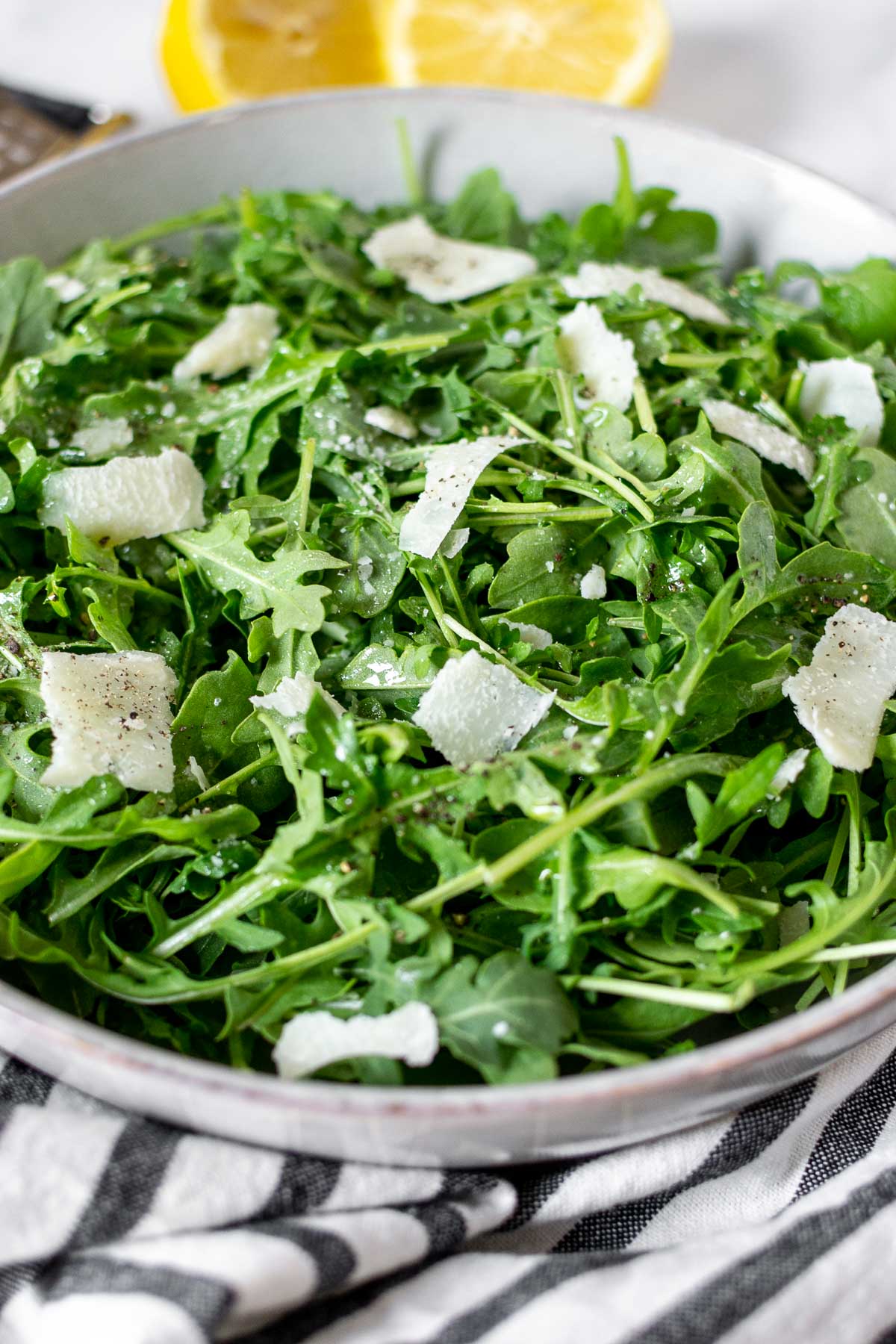 Close up to show texture of arugula salad with parmesan shavings and black pepper.
