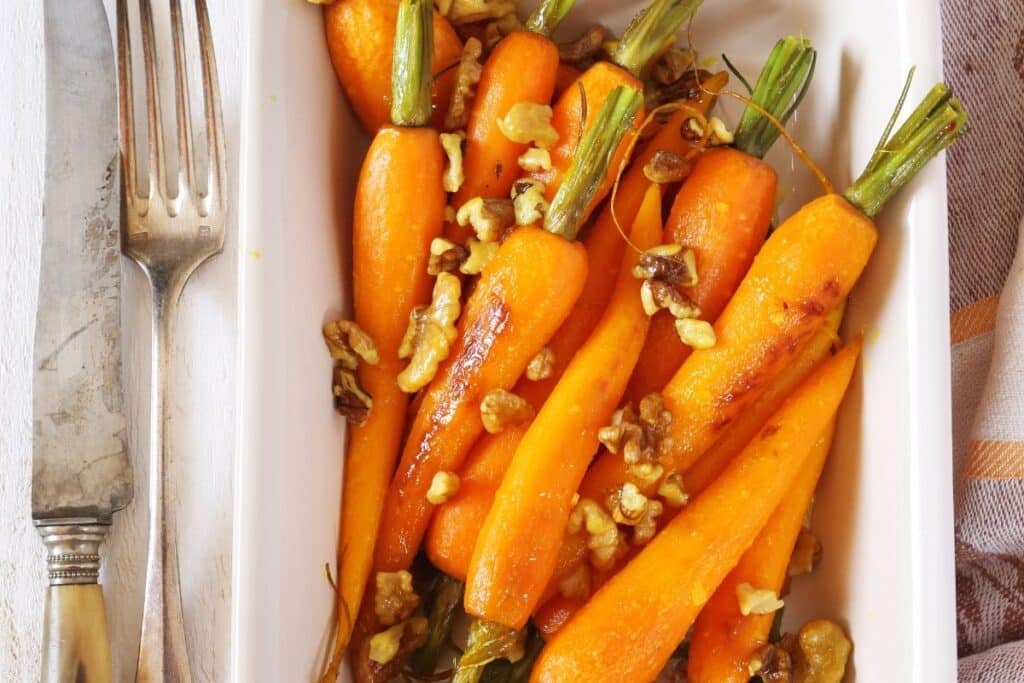 Roasted baby carrots on a white platter with a fork