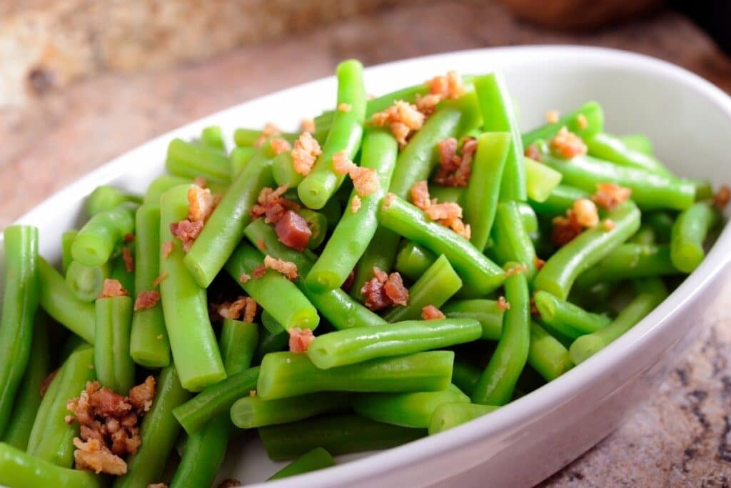 Green beans with bacon bits in a white bowl