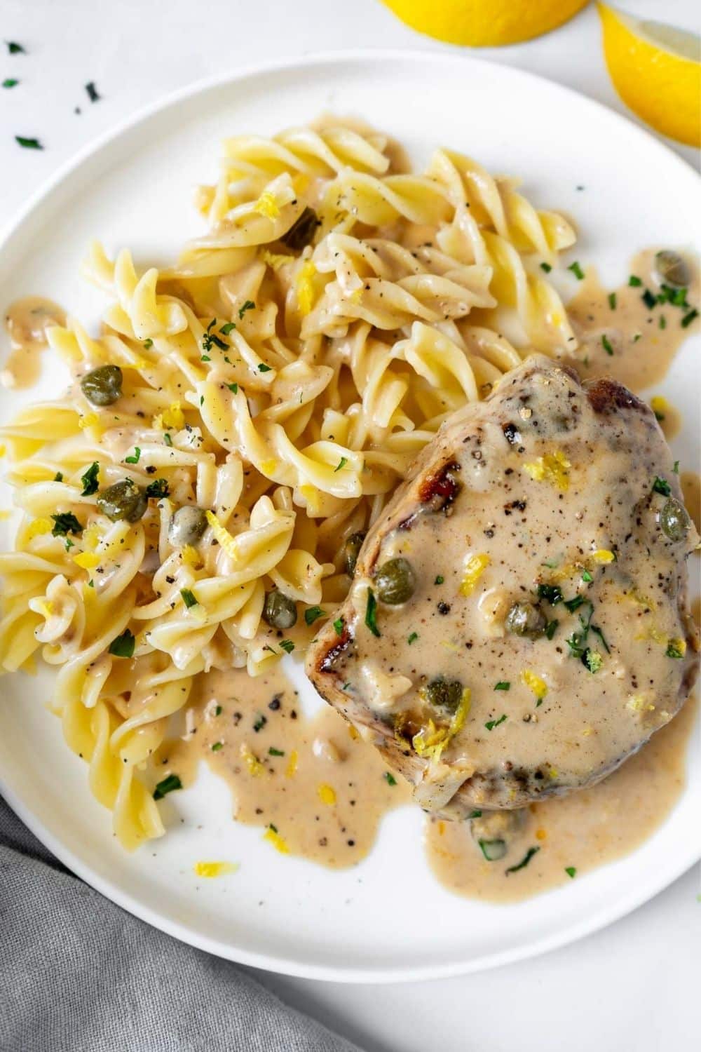 Pork chops with lemon caper sauce and pasta on a plate with lots of gravy