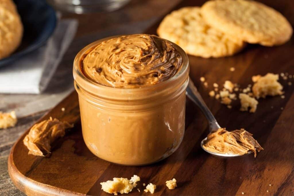 A small jar of cookie butter with a spoon and cookies around.