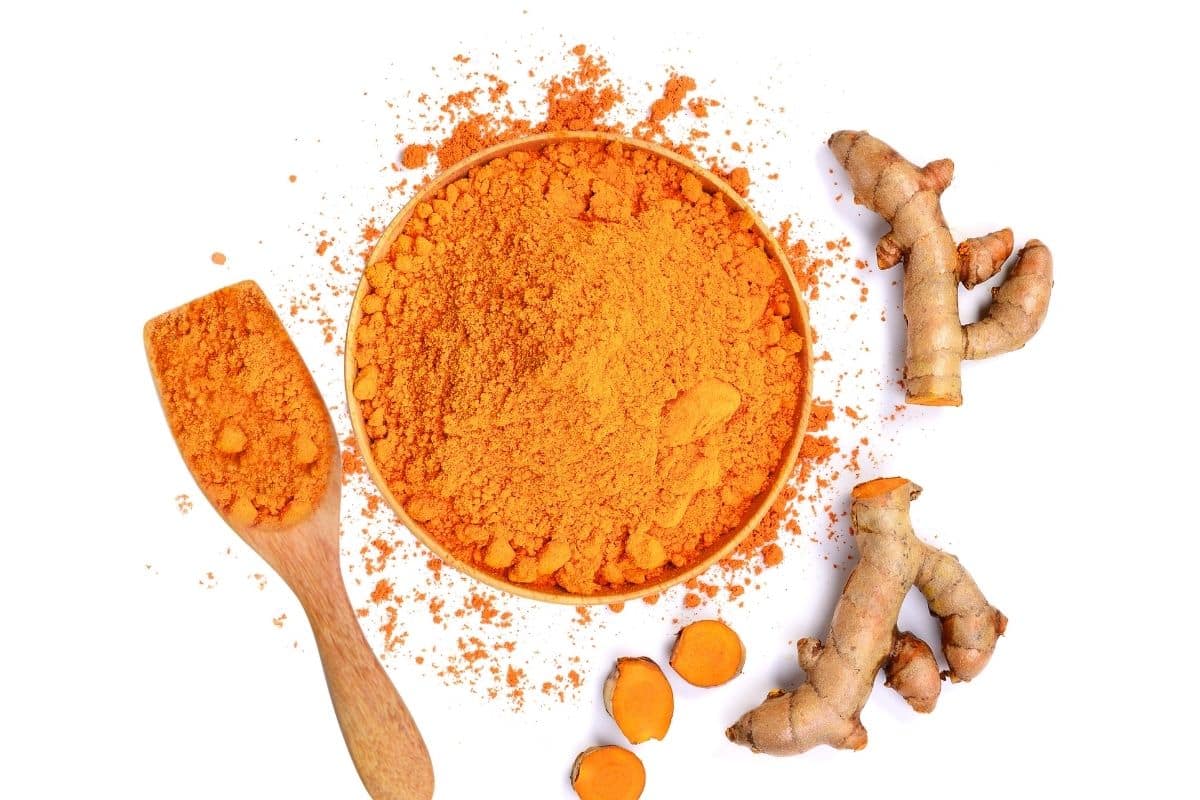 Ground turmeric in a bowl spilled out on a white background.