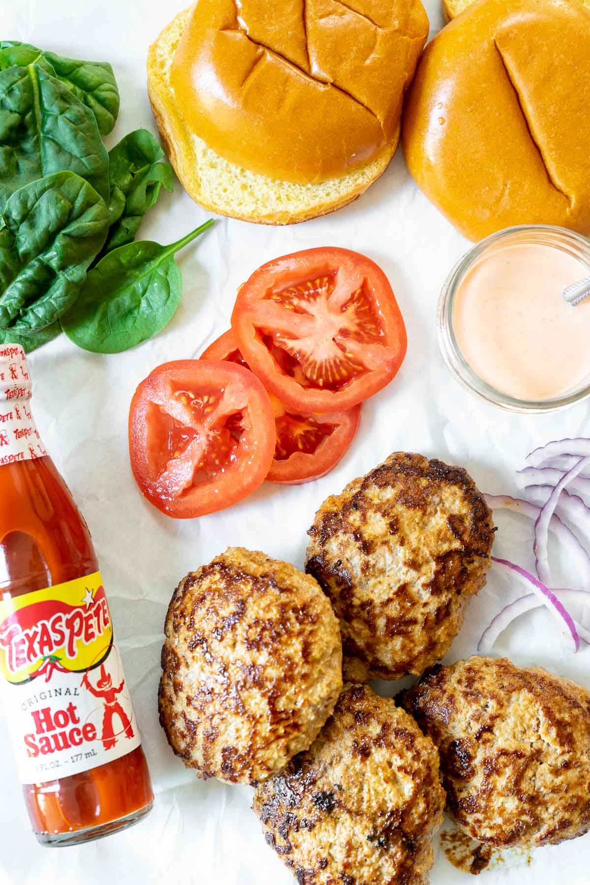 Turkey burgers and all toppings on a table with Texas Pete® Hot Sauce