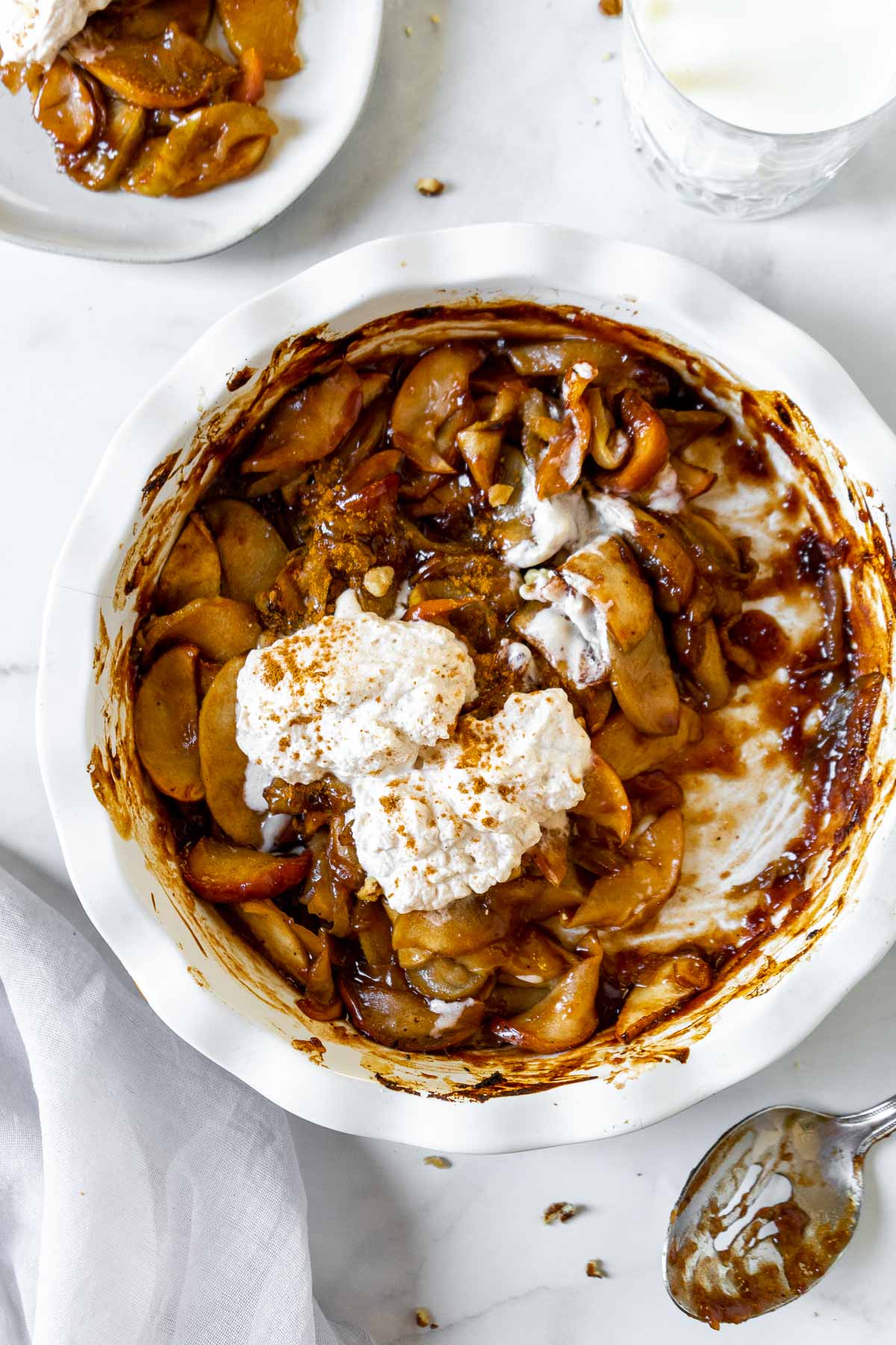 Air fryer baked apples in a large white baking dish topped with cinnamon whipped cream.