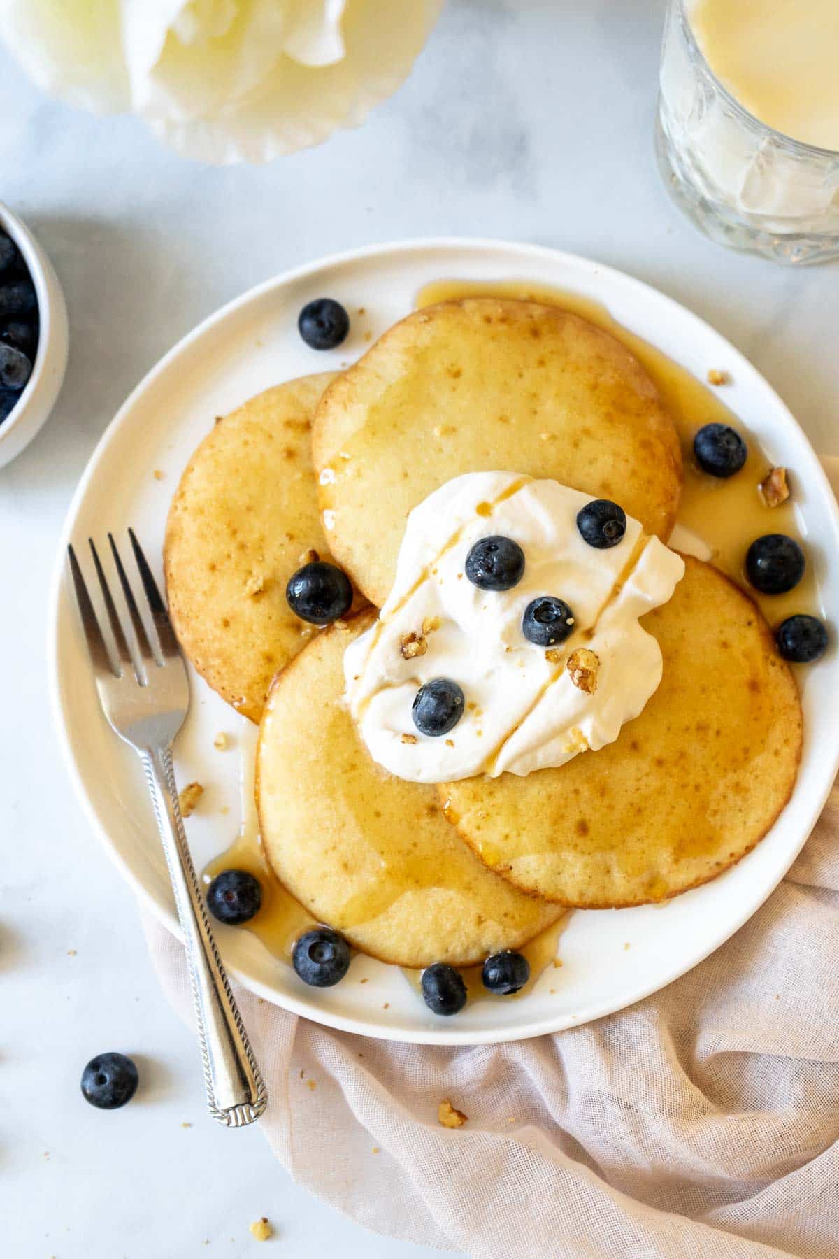 Four air fryer pancakes on a plate with whipped cream, blueberries and maple syrup.