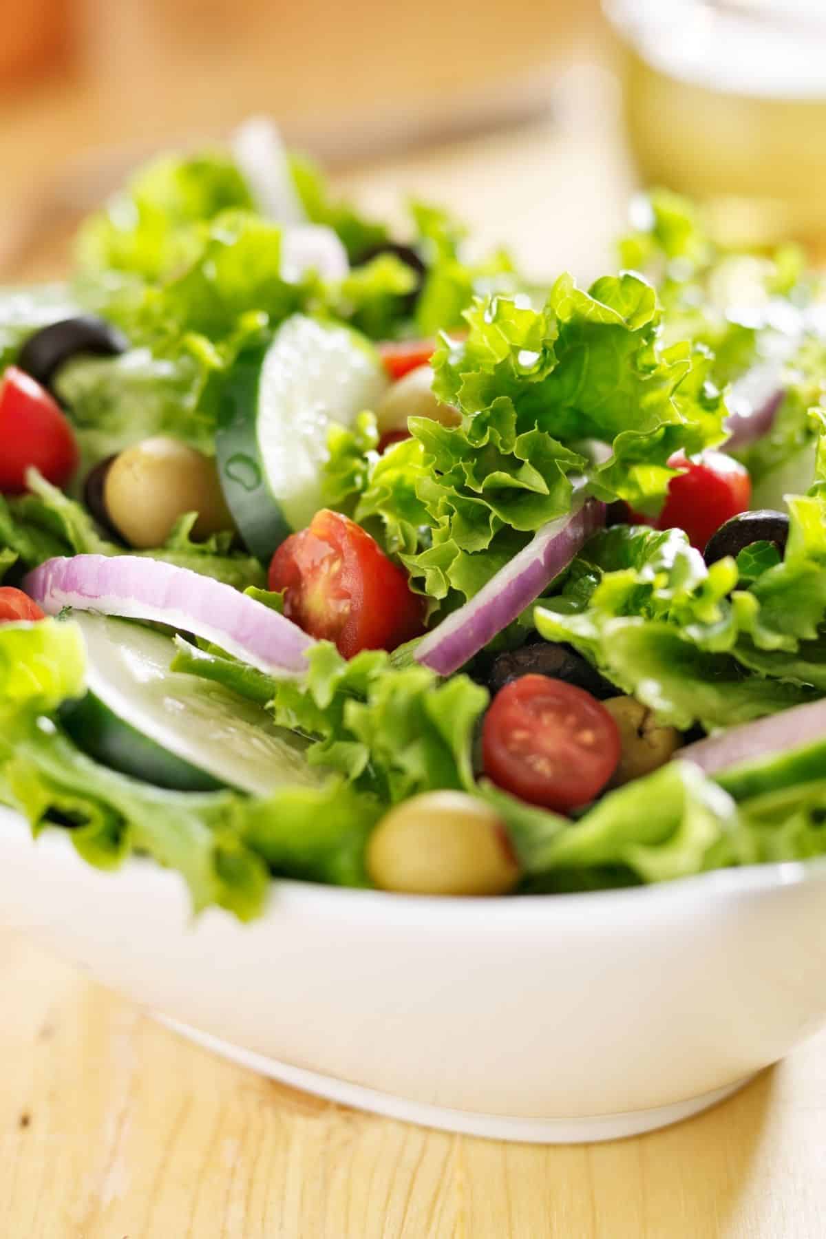 Close up of a simple green salad with tomatoes, red onions and olives.