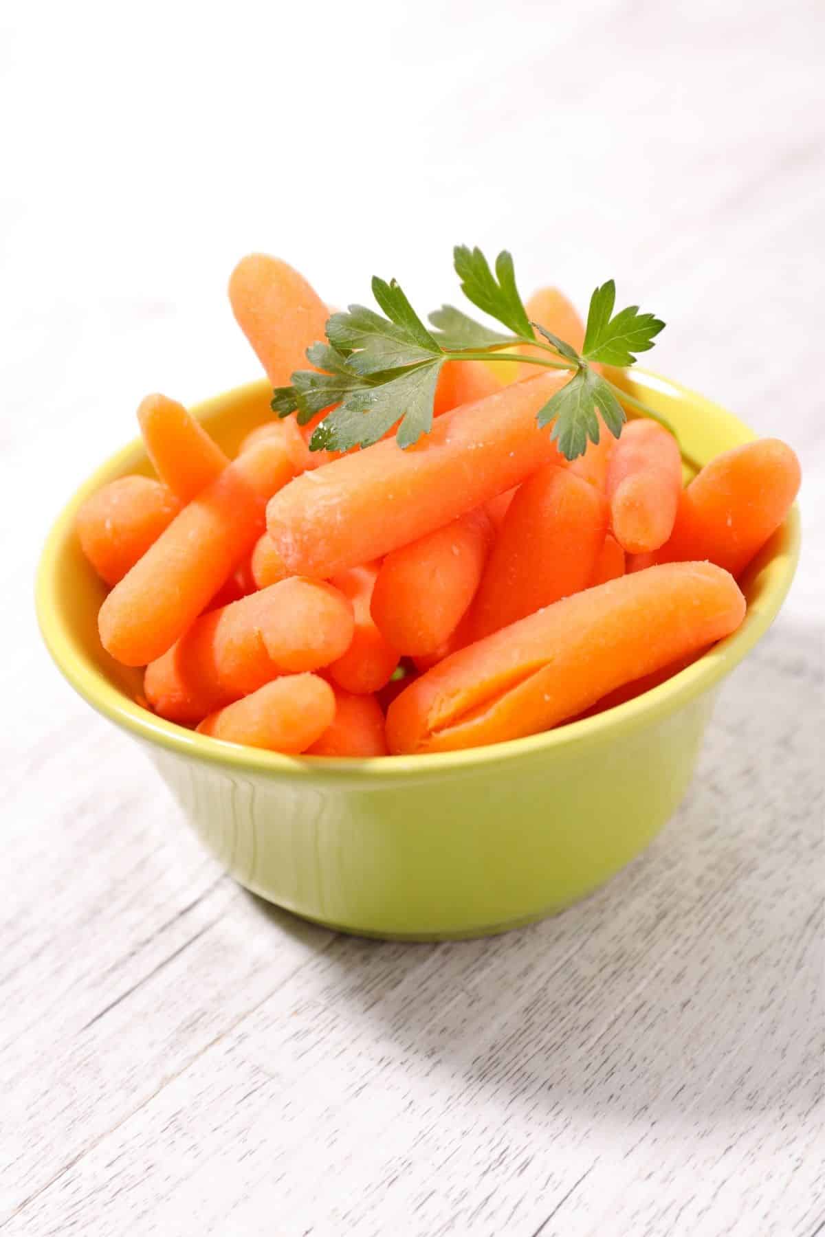 Baby carrots in a small yellow bowl with a sprig of parsley.