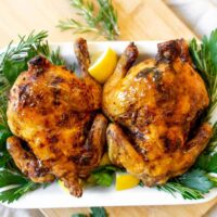 Two Cornish hens on a platter with greens and lemon.