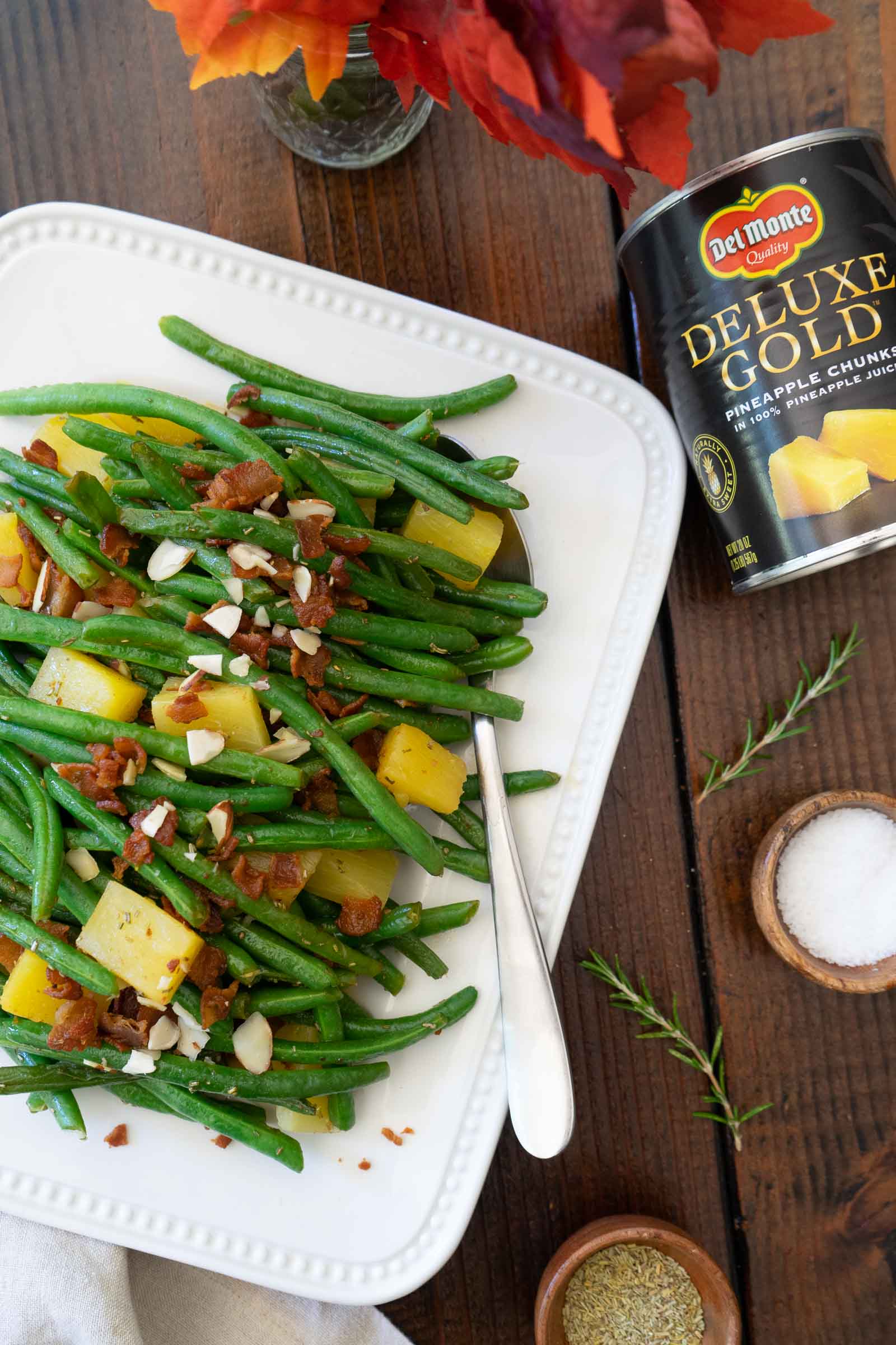 Green beans with pineapple and bacon on a platter , topped with almonds and a Del Monte Pineapple can in the corner.