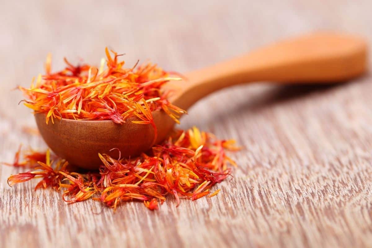 Alternatives to turmeric: Safflower on a spoon on a wooden background.