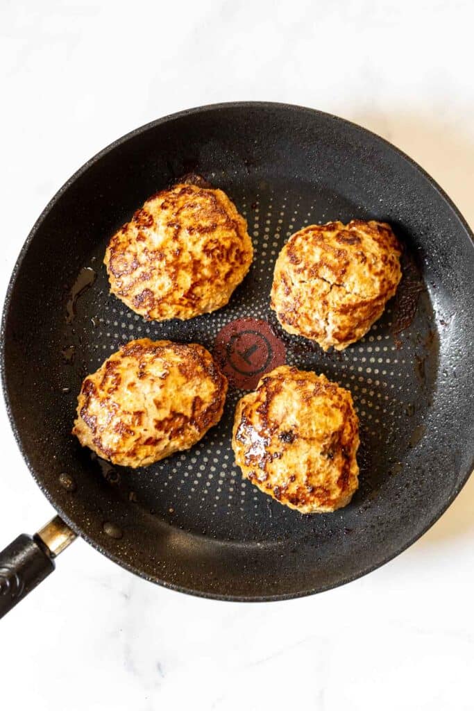 Spicy turkey burgers in a skillet being browned.