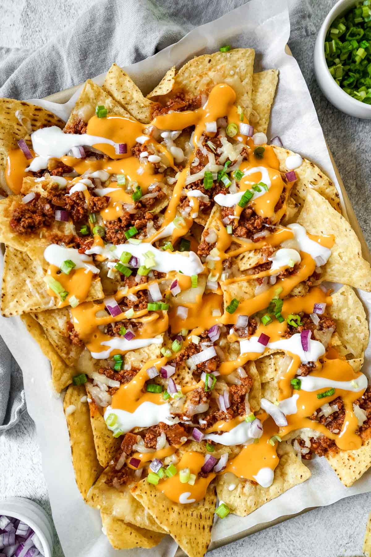 Chili con carne nachos on a baking sheet topped with onions, cheese and sour cream.