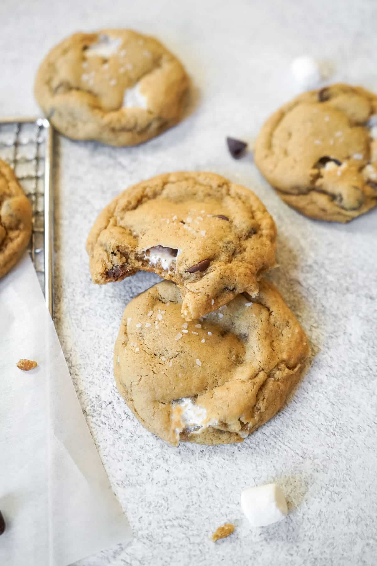 Several chocolate chip marshmallow cookies, one with a bite taken out of it. 