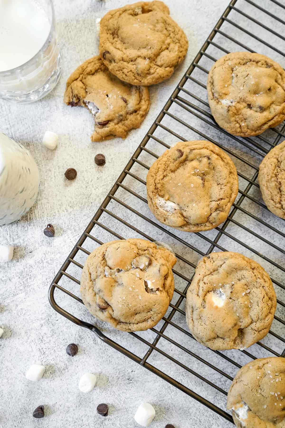 Several chocolate chip marshmallow cookies on a cooling rack with milk.