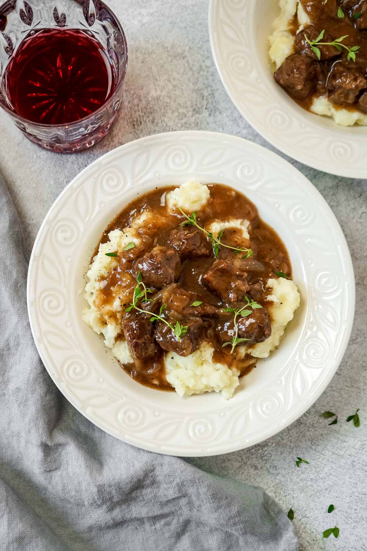 A bowl of beef tips cooked in the instant pot with gravy and a glass of red wine.