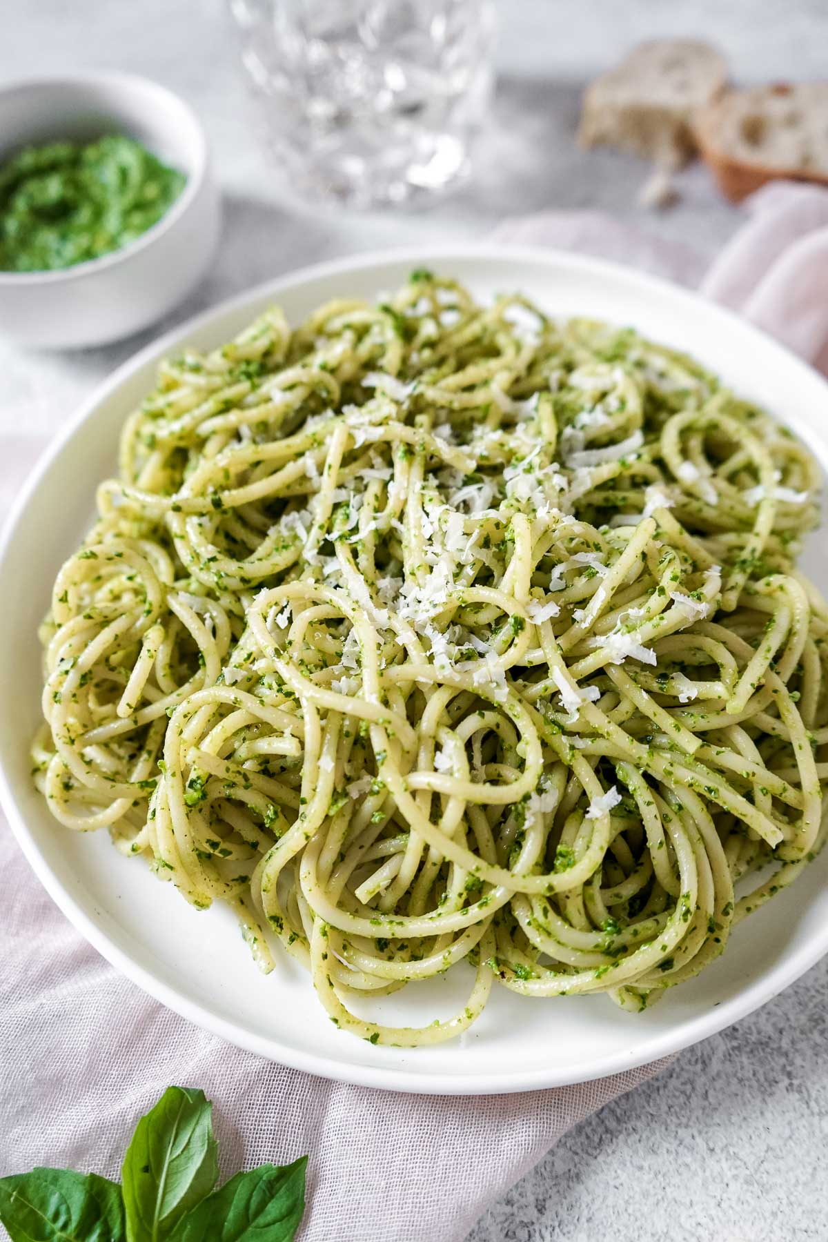 Pasta with green sauce on a white plate sprinkled with Parmesan cheese. 