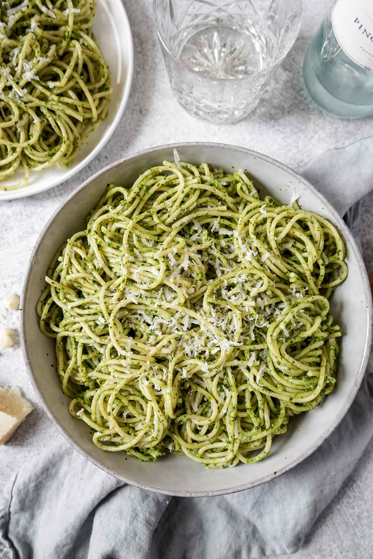A large bowl of pasta with green sauce sprinkled with Parmesan cheese.