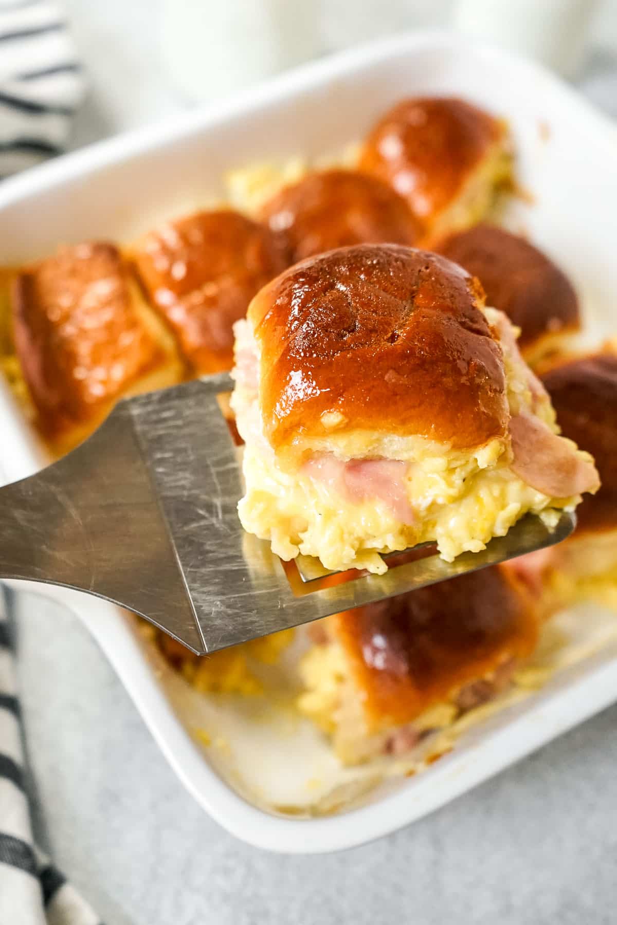 Pan of Hawaiian Roll breakfast sliders with one slider up close on a spatula.
