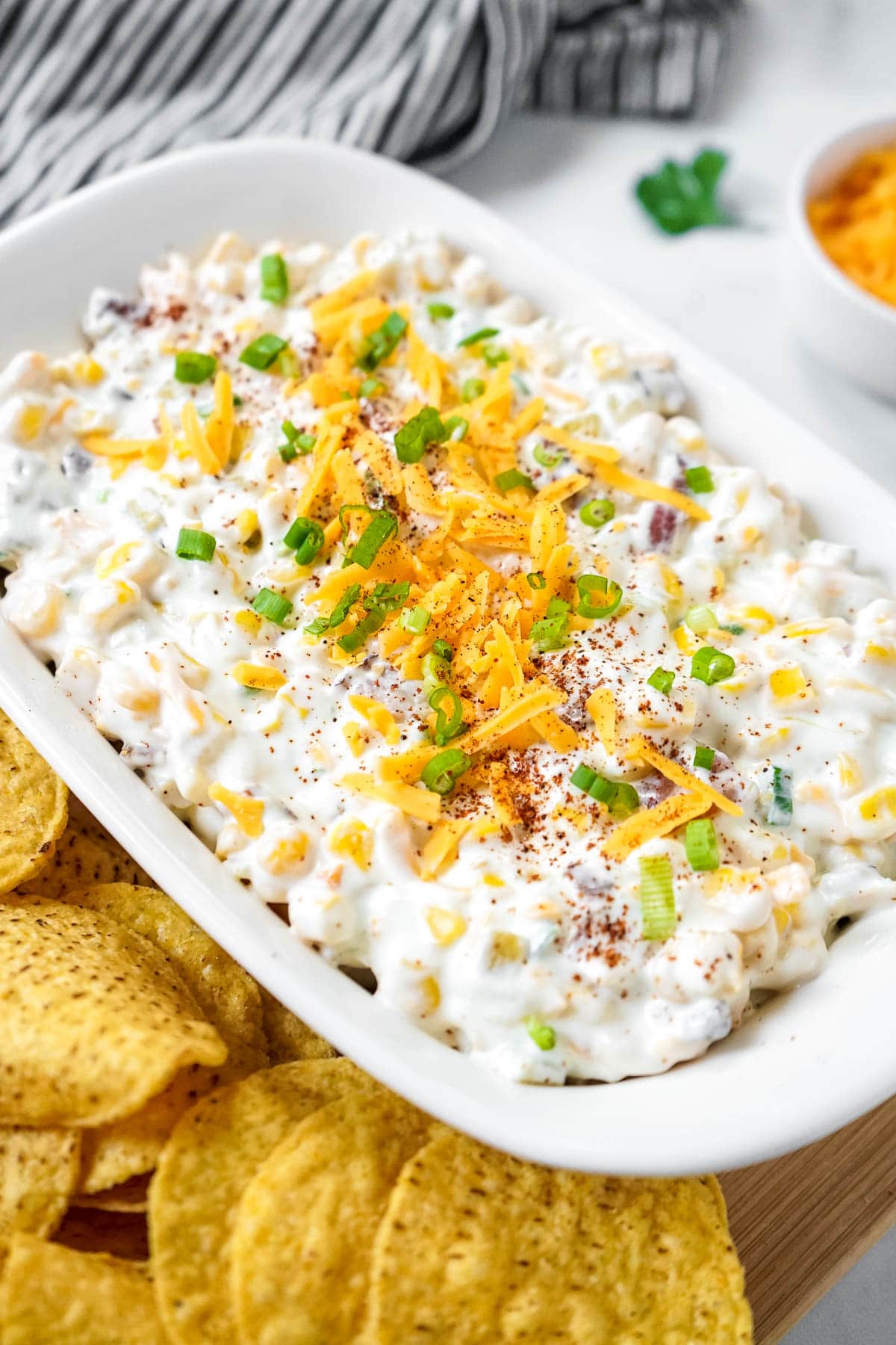 Bacon and corn crack dip in a serving dish sprinkled with chili powder, served with tortilla chips.