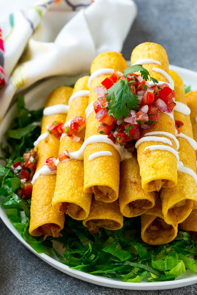 A large platter with taquitos stacked on top of each other and topped with salsa. 