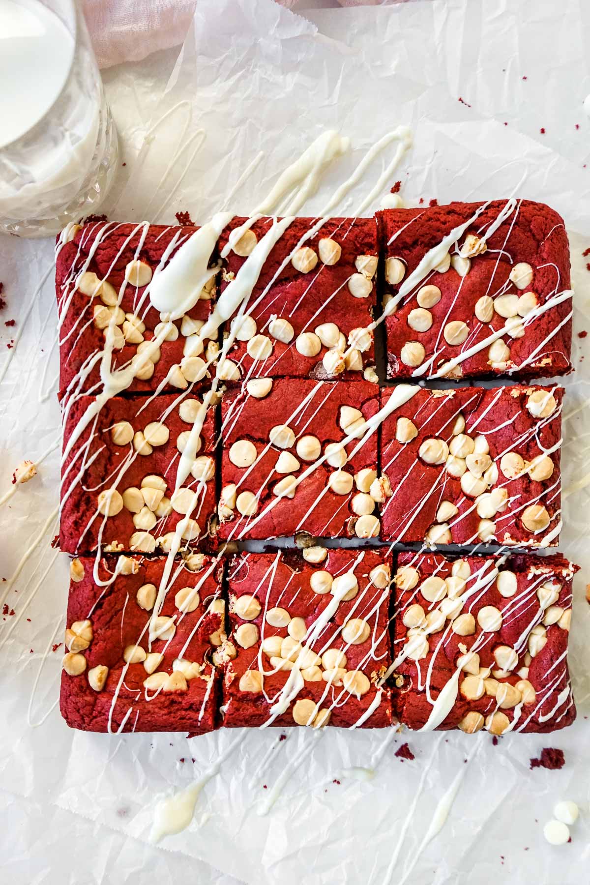 Red Velvet Brownies with White Chocolate Chips on a table drizzled with white chocolate.