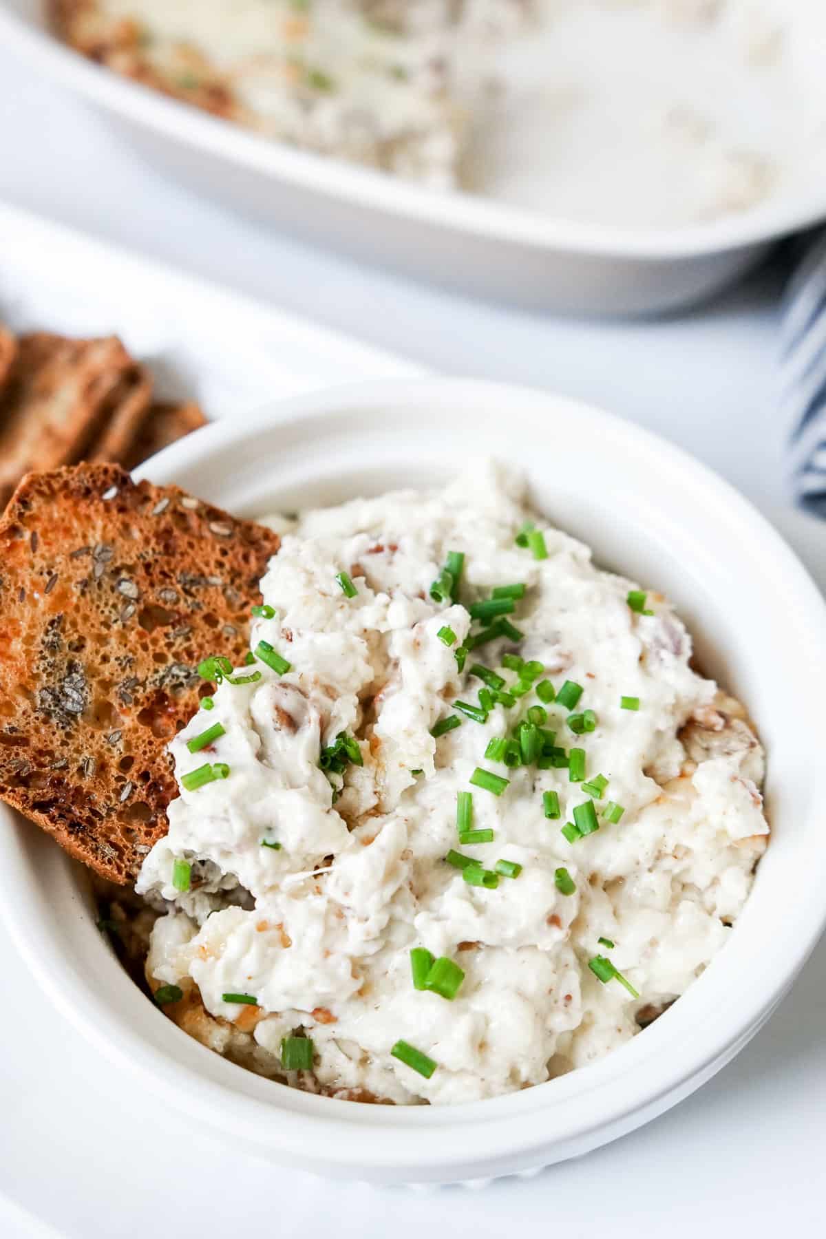 Swiss and bacon dip in a small white dish with a cracker. 