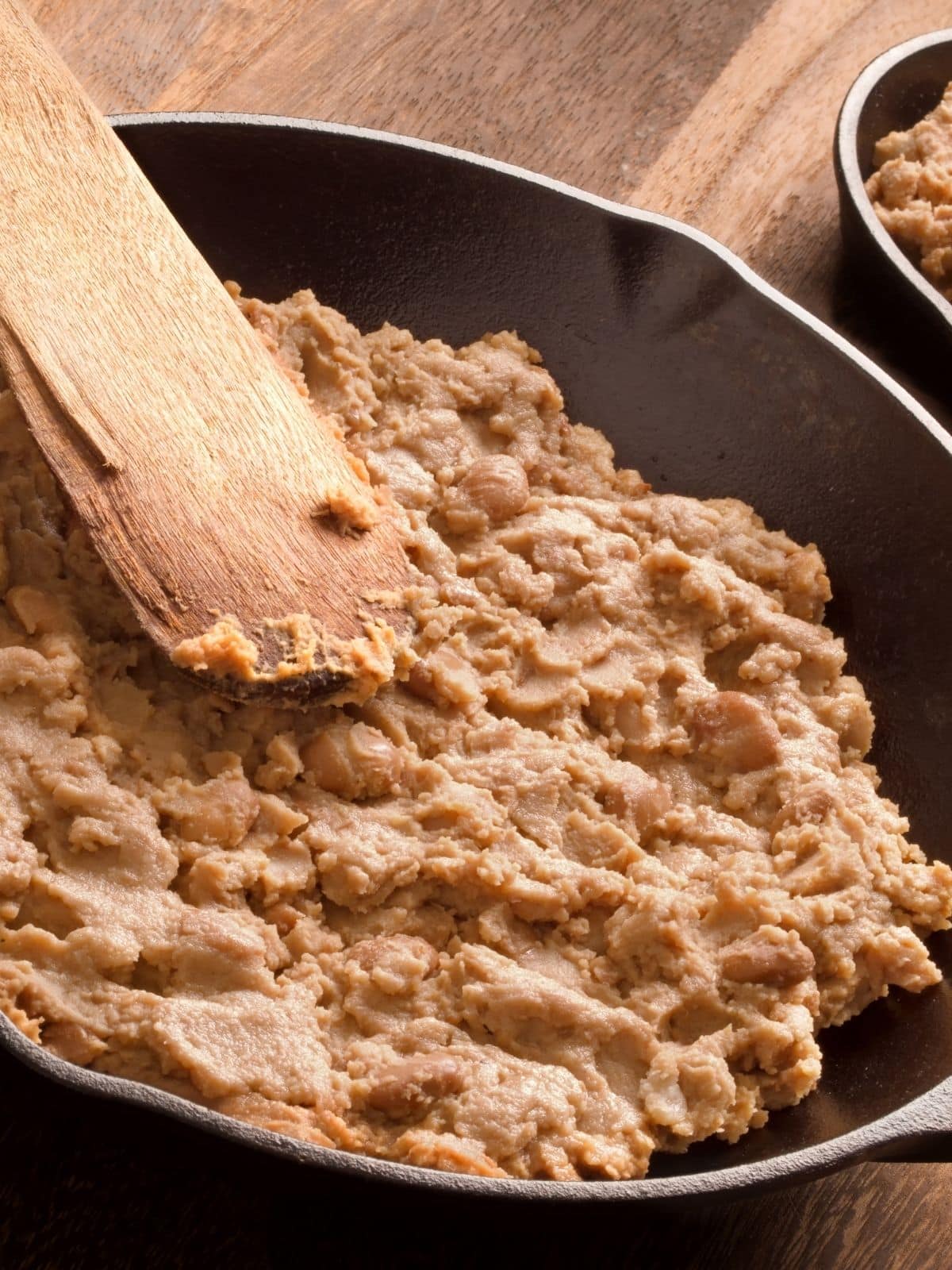 Refried beans are a traditional topping for nachos. Refried beans being cooked in a pan.