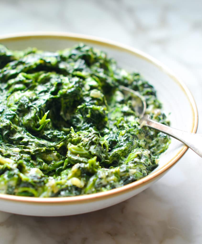 A bowl of creamed spinach with a spoon.