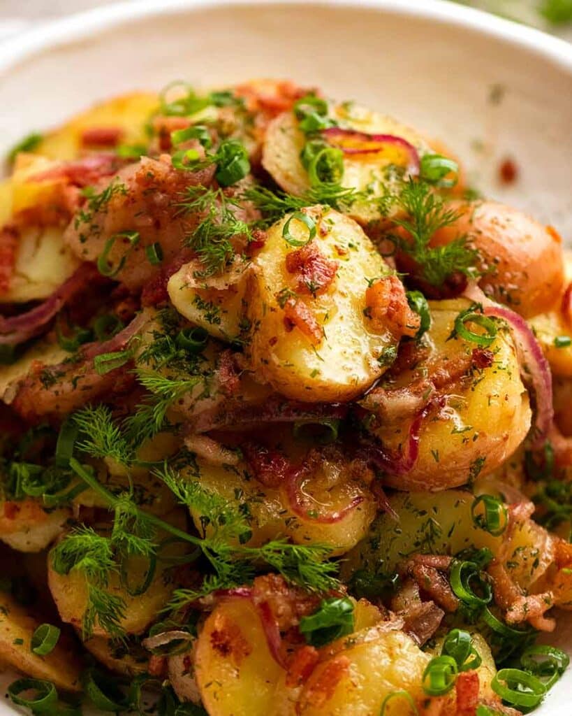 German potato salad in a large bowl topped with bacon and dill.