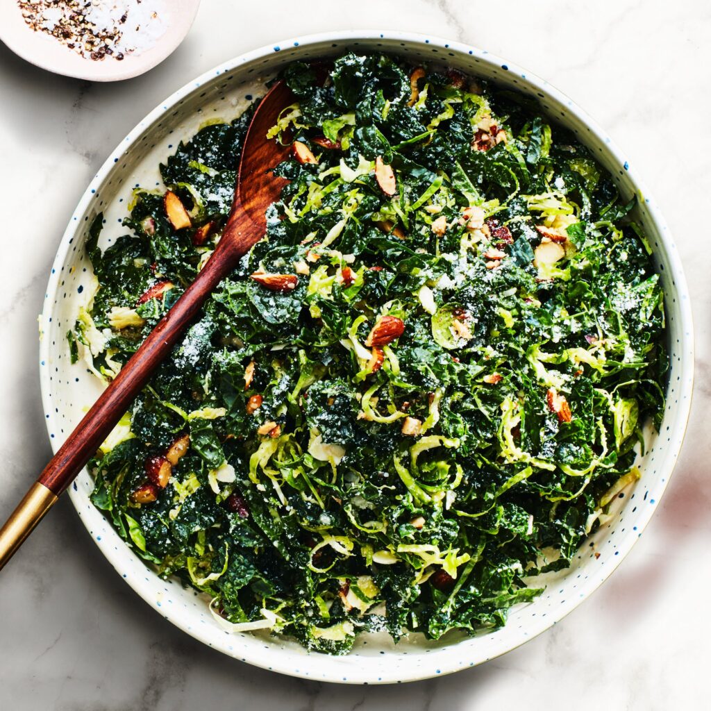 A dish with a kale and brussels sprout  salad with a wooden spoon.